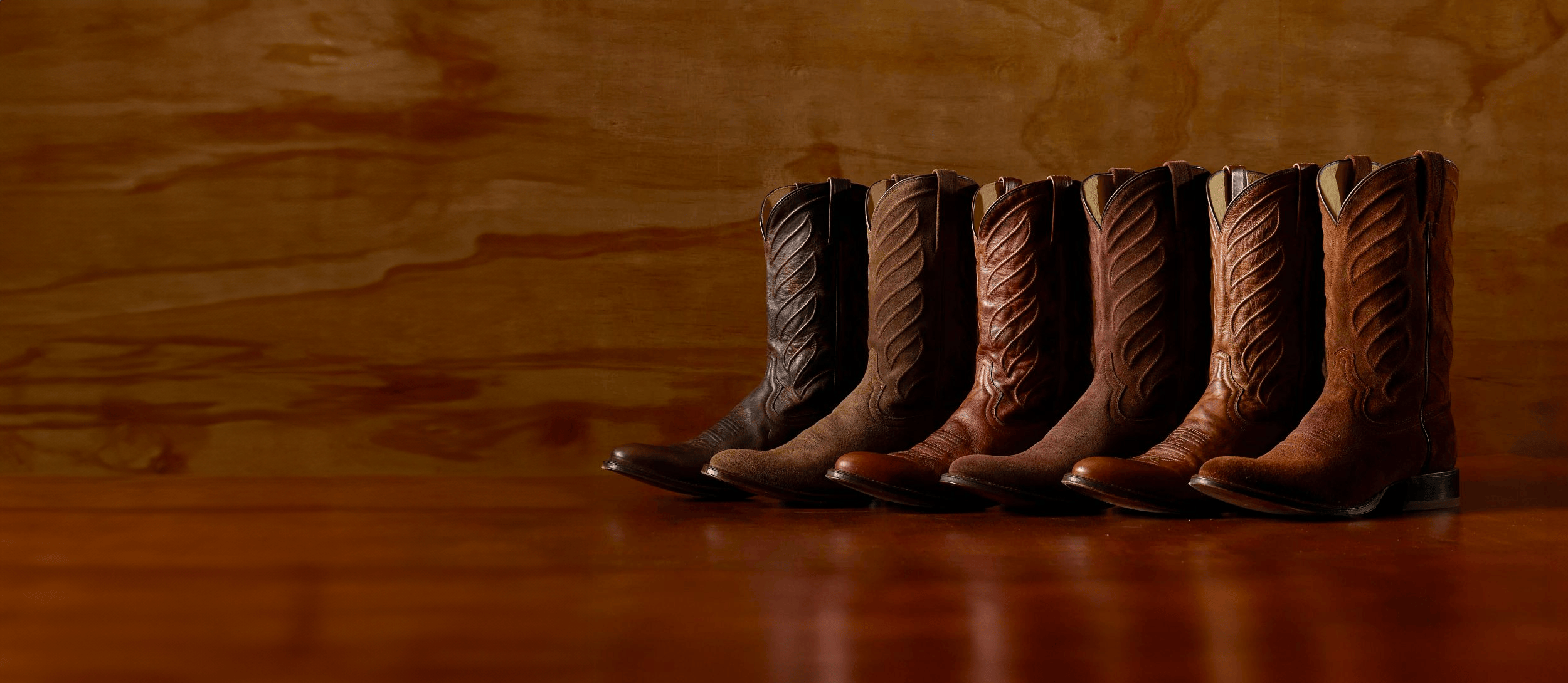 A lineup of Derby western boots in various colors on a wood surface. Shop the Derby Collection.